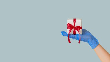 Hediye teslimatı hijyeni. Yeni yıl sürprizi. Koruyucu eldivendeki kadın eli mavi fotokopi arkaplanda izole edilmiş bir kutuya sarılmış mevcut durumu gösteriyor.