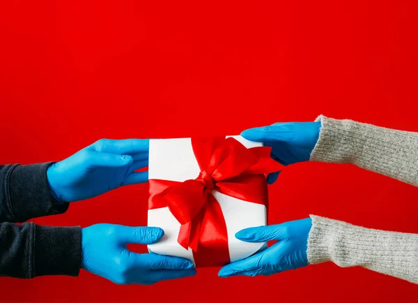 Gift offering. Handing present. Unrecognizable human hands giving in protective gloves wrapped box isolated on red free space background.