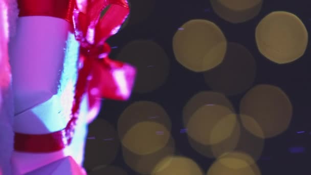 バーティカルビデオ クリスマスパッケージ ギフトラッピングデザイン 2つの現在のボックスは メリーライトの暗い背景に落ちる木の枝の冬の構成雪に赤いリボン弓をタップしました — ストック動画