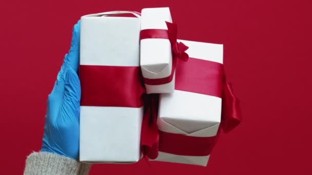 バーティカルビデオ ギフトデリバリー 伝染病が発生する 赤いコピースペースの背景に隔離された包まれた箱のロックダウン衛生を保持する保護手袋に4人の人間の手のセット — ストック動画