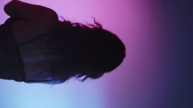 Dikey video. Dinamik dans. Çağdaş koreografi. Siyah dantelli, zarif, modern sanatçı kadın. Bulanık neon projektör arka planında hareket eden vücut..
