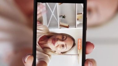 Dikey video. Etkileyici akış. Vlog kaydı. Neşeli kadın akıllı telefon ekranında çekim yapıyor. Işık odası içinde takipçilerle konuşuyor..