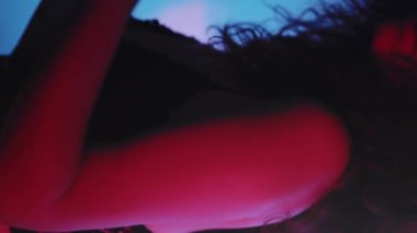 Dikey video. İç çamaşırı dansı. Kadınlık enerjisi. Siyah dantelli, zarif, çekici bir kadın bulanık, neon ışıklı arka planda hareket ediyor..