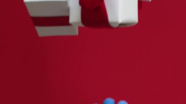 Dikey video. Virüs hazır. Pandemik doğum. Mavi koruyucu eldivenli eller, kırmızı arka planda izole edilmiş kış tatili indiriminden paketlenmiş hediye kutusunu alıyor..