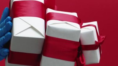 Dikey video. Salgın hediyeler. Noel hediyeleri. Mavi koruyucu eldivenli eller kırmızı arka planda karantina kış tatili indirimli kutuları gösteriyor..