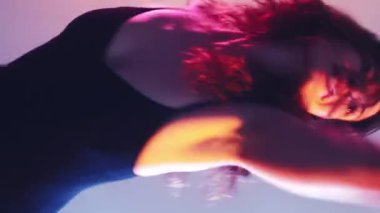 Dikey video. Vücut performansı. Çağdaş dans. Şehvetli profesyonel plastik esnek koreograf kadın neon ışıklı arka planda hareket ediyor.
