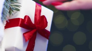 Dikey video. Mutlu noeller. Hediye sürprizi. Xmas dekorasyonu. Kadın el ele tutuşup kırmızı fiyonklu hediye kutusunu kışın kar çamı kompozisyonu Bokeh 'in arka planına koyuyor..