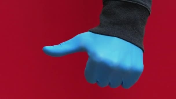 バーティカルビデオ パンデミック紛争 クォンタインジェスチャー 赤い背景で隔離された反対の承認の不一致の印を示す青い保護手袋の手 — ストック動画