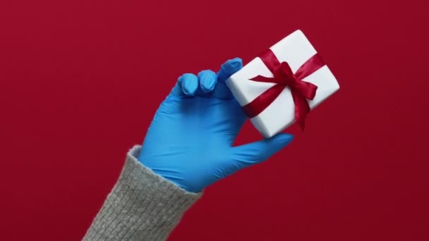 バーティカルビデオ プレゼント配信 伝染病の贈り物 保護グローブに認識できない人間の手 包まれた箱の隔離衛生措置 赤い空のスペース背景で隔離 — ストック動画