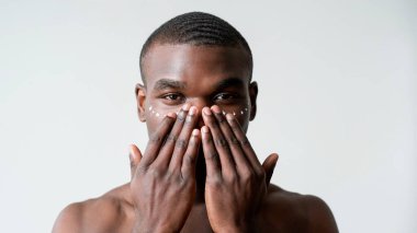 Erkek kozmetiği. Cilt nemlendirici. Beyaz arka planda izole edilmiş gözlerin altında yaşlanma karşıtı cilt kremi kullanan kendinden emin bir adam..