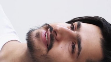 Dikey video. Gülen surat. Dişli gülümseme. Keyfin yerinde. Çekici, neşeli, sakallı adam beyaz arka planda olumlu duygular ifade ediyor..