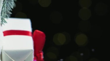 Dikey video. Noel tatili. Şenlikli hediye dekoru. Yeni yıl kutlaması. Mevcut kutu, kışın çam dalına bantlanmış kırmızı kurdele yayıyla sarılı. Arkaplanda parıldayan ışıklar var..