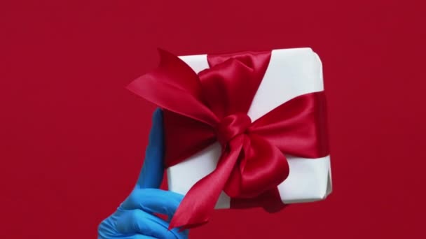 バーティカルビデオ プレゼント配信 ホリデーギフト 赤い背景に隔離されたジェスチャーのような包まれた箱の親指を握る保護手の認識できない人間の手 — ストック動画
