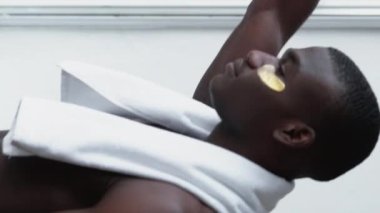 Dikey video. Metroseksüel yaşam tarzı. Sabah bakımı. Kendine güvenen, altın gözlü, üstsüz, beyaz bantlı, gülümseyen, camdan dışarı bakan, pürüzsüz tenli bir adam..