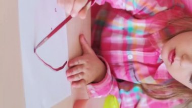 Dikey video. Anaokulu resmi. Yaratıcı aktivite. Hevesli bir kız çocuğu anaokulu masasında sanatçı hobisi yaparken eğleniyor..
