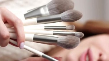 Dikey video. Makyaj aletleri. Fırça takımı. Güzel aksesuarlar. Sarışın kadının elleri göz farı pudrası allık yüz derisi için makyaj malzemesi koleksiyonu..
