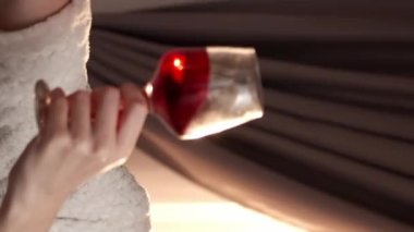 Dikey video. Çevrimiçi içki. Sanal arama. Uzaktan kutlama. Bornozlu mutlu bir kadın, şarap kadehiyle selamlıyor telefon kamerasından konuşuyor..