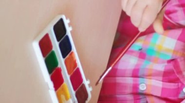 Dikey video. Çocuk sanatı. Anaokulu aktivitesi. Küçük kız, yaratıcılık geliştirme dersinde masada boya fırçasıyla suluboya resim çiziyor..