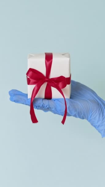 バーティカルビデオ ギフトデリバリー衛生 新年サプライズ 青いコピースペースの背景に隔離された箱に包まれていることを示す保護手袋の4つの手のセット — ストック動画