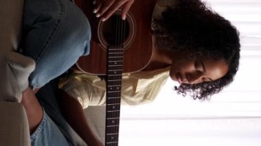 Dikey video. Gitar çalmayı öğrenme. Müzik dersi. Uzaktan eğitim. Çalışkan kadın gitarist ev koltuğunda dizüstü bilgisayarda pratik yapıyor..