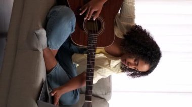 Dikey video. Çevrimiçi müzik okulu. Gitar dersi. Uzaktan öğrenme. Kadın gitarist dizüstü bilgisayarda ip enstrüman akorları pratiği yapıyor..