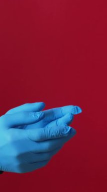 Dikey video. Salgın var. Hediye teslimatı. Mavi koruyucu eldivenli eller. Kış tatili paketlerini almaya korkuyorlar. Sosyal mesafeler kırmızı boş alanda izole edilmiş..