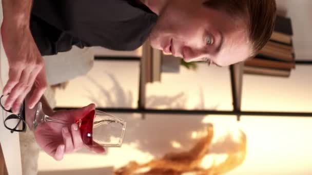 バーティカルビデオ オンラインドリンク アルコールチャット バーチャルコール 近代的な家庭の職場のインテリアでラップトップで話す赤ワインのガラスを持つ落ち着いた自信あるビジネスマン — ストック動画