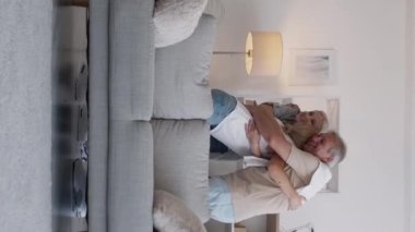 Dikey video. Aile toplantısı. - Kız öğrenci. Keyifli bir an. Mutlu bir anne ve baba kızı kucaklıyor. Açık bir evde koltukta oturuyor..