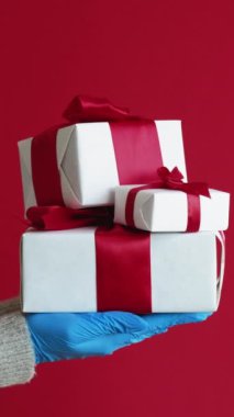 Dikey video. Doğum günü hediyesi. Teslimat hazır. Plastik eldivenler içinde tanınmayan bir insan eli. Paketlenmiş koronavirüs koruyucu giysiler. Kırmızı serbest alan arka planında izole edilmiş..