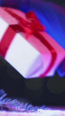 Dikey video. Xmas selamı. Teslimat koruması. Tıbbi eldivenleri verin. Çam dalında kırmızı kurdeleli kutuyu sallayın. Arka planda kar fırtınası var..