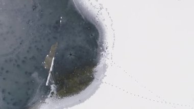 Dikey video. Üstgeçit kışı. Drone donmuş göl. Bulutlu bir sabahta kırsal nehir manzaralı buz birikintileri olan karlı bir zemin..