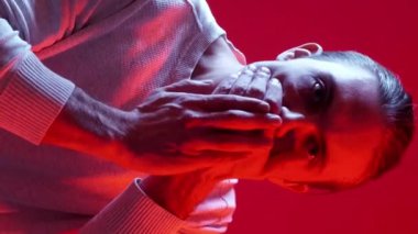 Dikey video. Sessiz ol. Sessiz ol uyarısı. Mavi kırmızı renkli, neon ışıklı, ağzı kapalı rahatsız bir adam..