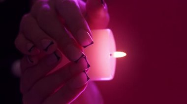 Dikey video. Mum meditasyonu. Dua geleneği. Kadın ellerinin parlak pembe neon ışıkta yanan mum ışığını tuttuğu yakın plan.