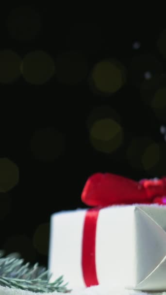 垂直录像 圣诞节假期 节日礼物装饰 新年庆祝活动 冬松枝叶雪光闪烁的背景上 用纸盒包裹着红丝带弓 — 图库视频影像