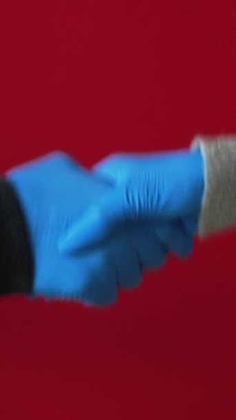 バーティカルビデオ コロナウイルス挨拶 パンデミックハンドシェイク 赤いコピースペースの背景に隔離された青い保護手袋で挨拶する3人の男の女性のセット — ストック動画
