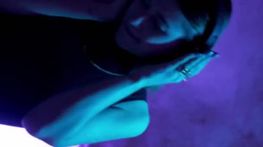 Dikey video. Müzik zevki. Kablosuz kulaklıklar. Gece eğlencesi. Kaygısız dans eden kadın canlı renkli ışıklı duman efektiyle tekno şarkı listesi dinliyor..