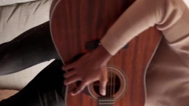 Dikey video. Gitar keyfi. Müzik çalıyor. Neşeli yetenekli genç adam evdeki kanepede akustik telle şarkı söylüyor..
