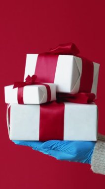 Dikey video. Hediye teslimatı. Salgın hastalık belirtileri. Koruyucu eldivenli dört insan eli kırmızı fotokopi arka planında izole edilmiş kilitli kutular..