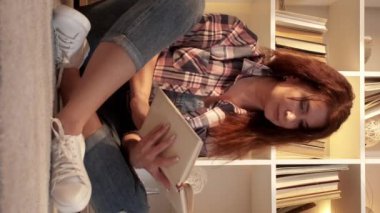 Dikey video. İlginç bir kitap. İlham verici bir kadın. Ev tatili. Orta yaşlı bir kadın yerde oturuyor ve aydınlık odada kitap okumaktan zevk alıyor..