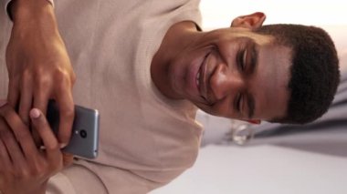 Dikey video. Gezici eğlence. Gadget sohbeti. İnternet taraması. Akıllı telefondan mesaj atan mutlu, rahat adam evde internet üzerinden iletişimin keyfini çıkarıyor..