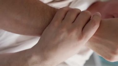 Dikey video. Ağrılı eklemler. Yaşlı adam. Yaş değişir. Tanımlanamayan yaşlı erkek masajcı eller uyuşmuş bir şekilde kanepede oturuyor..