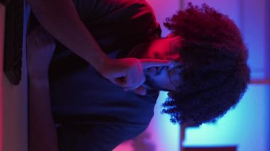 Dikey video. Sessiz ol. Sessiz adam. Meme ifadesi. Hippi adam ağzında şşşş parmağını tutuyor. Neon ışıklı odada masasında oturuyor. İçi döngü dolu..