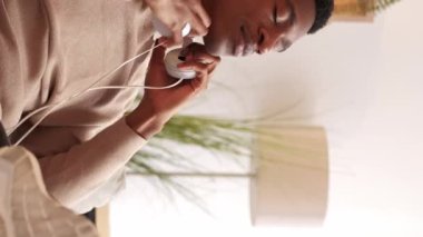 Dikey video. Şarkı sevinci. Müzik aleti. Ses eğlencesi. Kulaklıkla en sevilen müzik listesini dinleyen mutlu adam evdeki oturma odasında ellerini kaldır..