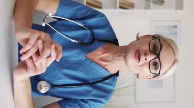 Dikey video. Çevrimiçi toplantı. Kadın bir doktor. Sanal selamlama. Medikal giysiler içindeki ilham verici kadın masa lambasının içindeki meslektaşına el çırpıyor..