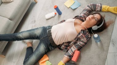 Ev temizliği. Yorgun yetişkin kadın. Müzik ilhamı. Kulaklıklı, yorgun bir kadın. Işıklandırma odasındaki temizlik personelini çevreleyen yerde yatıyor..