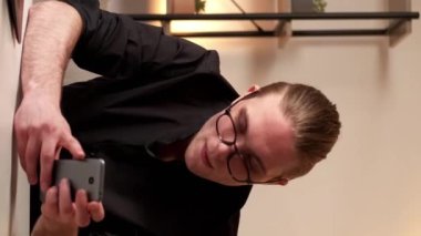 Dikey video. Dijital iş. Çevrimiçi yönetim. Uzaktan kumanda. Kendine güvenen, gözlüklü, modern ofis işyerindeki dizüstü bilgisayarla çalışan zeki bir adam..