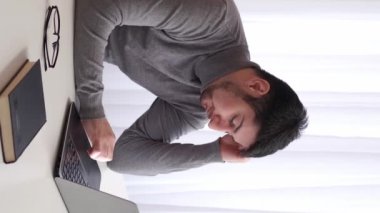 Dikey video. İş baskısı. Yorgun bir çalışan. İş yorgunluğu. Yorgun ve mutsuz bir iş adamı, son teslim tarihine kadar uykusuzluk çektiğini ve modern ofis masasında uykusuz kaldığını vurguladı..