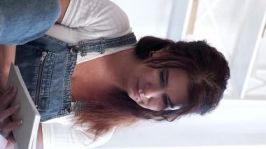 Dikey video. Okumaktan zevk alıyorum. Romantik kadın. Evde rahatla. Gülümseyen orta yaşlı kadın, kitap aydınlatma odasının sayfalarını çeviriyor..