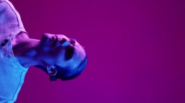 Dikey video. Neon insanları. Reklam arkaplanı. Bilgi sunumu. Mavi renkli ışık, mor boş alanda görünmez metin okuyan meraklı adam..