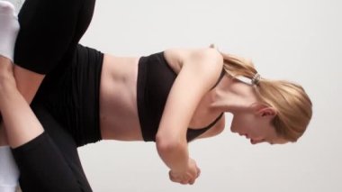 Dikey video. Sabah egzersizi. Evde fitness. Kapalı alan sporu. Gülümseyen atletik kız sırt kaslarını esnetiyor yerde bağdaş kurarak oturuyor..